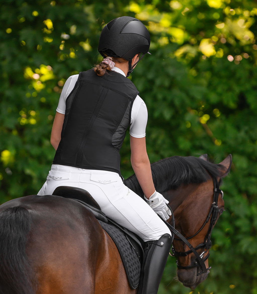 Person riding a horse in equestrian airbag vest with a blurred green background
